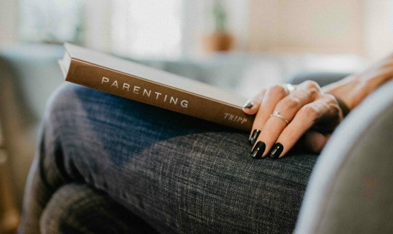 A woman holding a book while sitting on a couch.