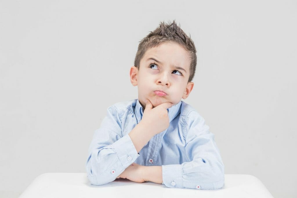A young boy at a table during a well child check, pondering with his hand on his chin.