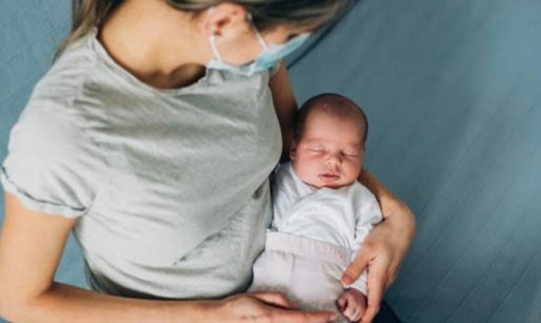 A woman holding a baby wearing a face mask to protect against coronavirus.