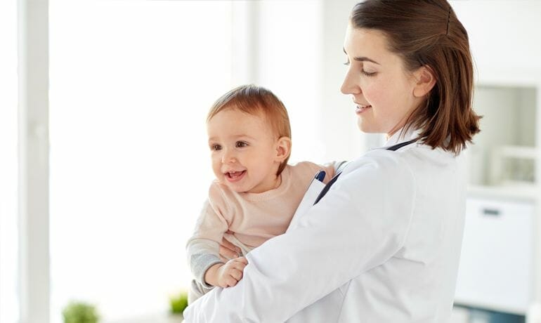 A woman cradling a baby, wondering when to get a pediatrician.