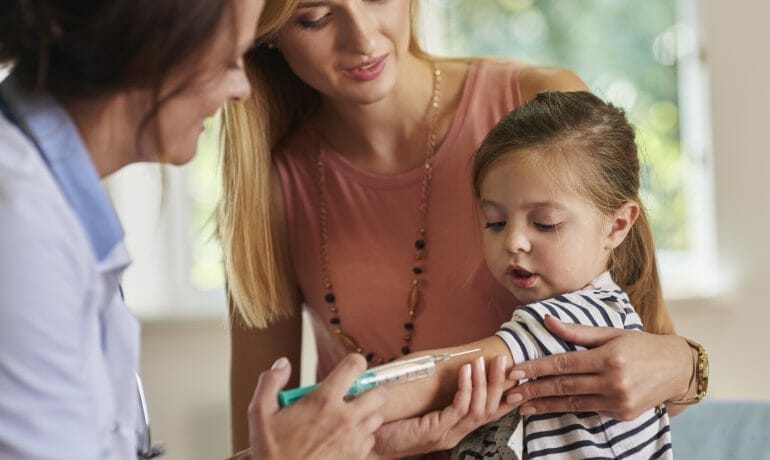 A young girl receives a flu shot during a doctor's examination amidst the COVID-19 pandemic.