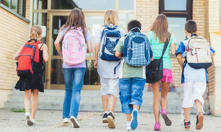 A group of children with backpacks walking out of a building.
