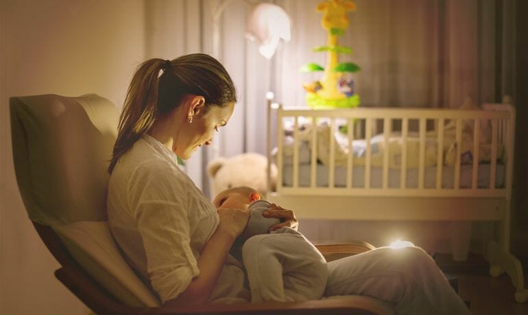 A mother peacefully breastfeeds her baby in a rocking chair, reaping the benefits for both.
