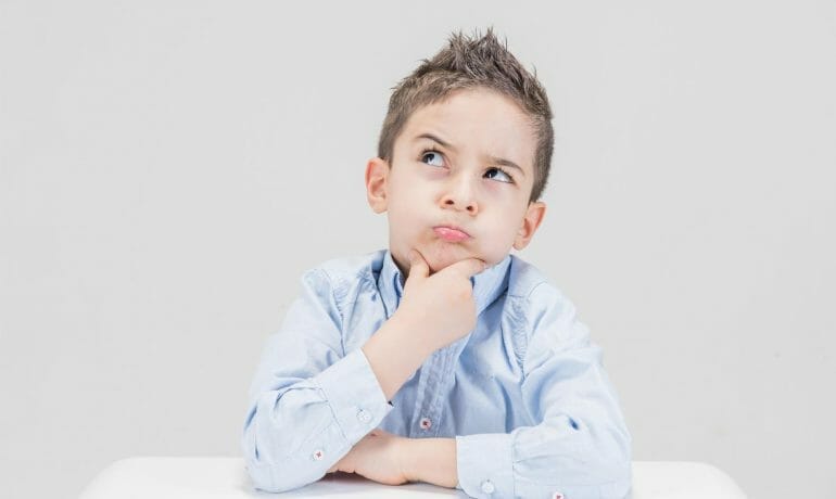 A young boy at a table during a well child check, pondering with his hand on his chin.