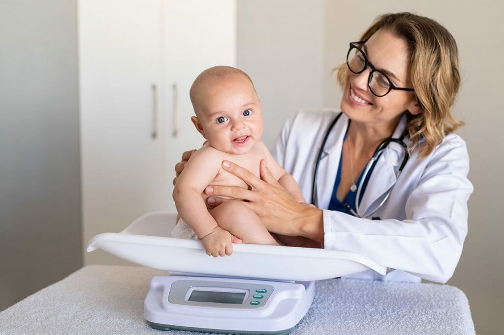 A pediatrician observes a woman weighing her baby at a clinic.