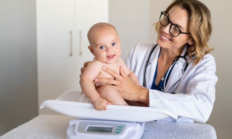 A pediatrician observes a woman weighing her baby at a clinic.