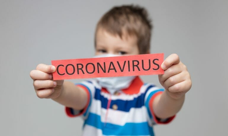 A young boy holding up a sign that says flu shot and COVID-19.