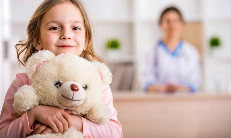 A young girl receiving care from one of the best pediatricians in Sugar Land, while holding a teddy bear.