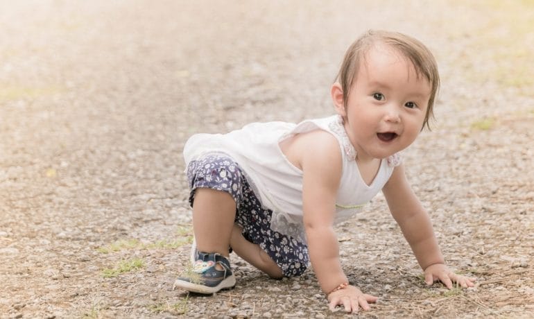 A baby crawling on a dirty road.