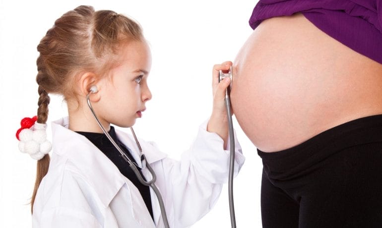 A little girl is observing a pregnant woman with a stethoscope to learn about prenatal health.