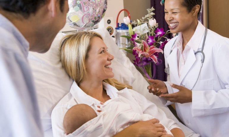 Women talking to a baby in a hospital bed while discussing pediatrician options.