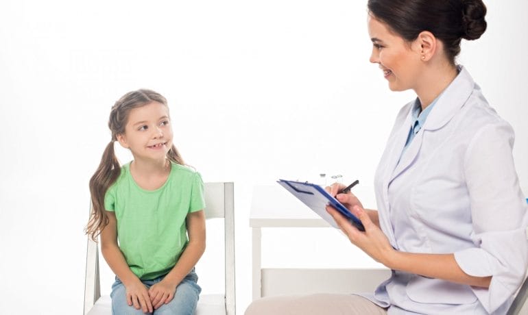 A doctor is talking to a little girl in a chair.