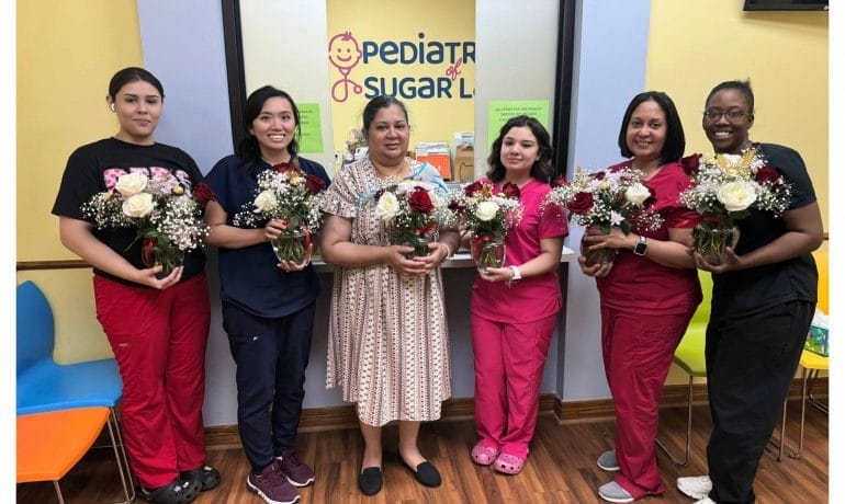 Five women standing in a pediatric clinic, each holding a bouquet of flowers, with colorful walls and a playful logo in the background.